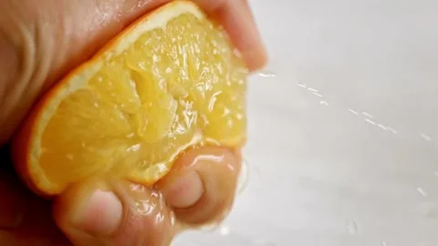 Close Up Hand Squeezing a Juicy Orange Fruit. Hand squeezing out fresh orange Stock Footage 265841313