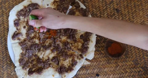 Close up of a hand squeezing lime and putting spices on Manakish Lahm Bi Ajeen - 스톡 동영상 151468128