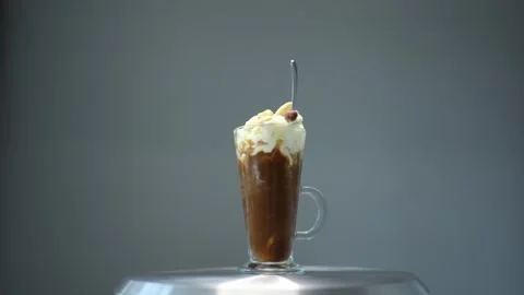 A close-up of a hand stirring a glass of coffee topped with whipped cream and ga Stock Footage 300021810