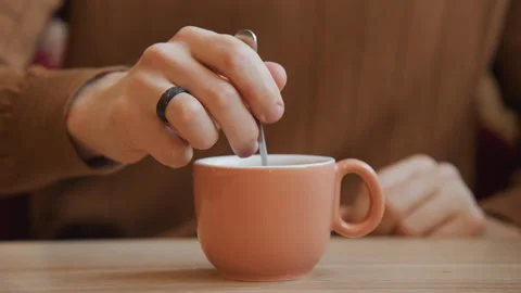 Close up hand stirring pink ceramic cup on wooden table with soft lighting with Vidéo 345730432