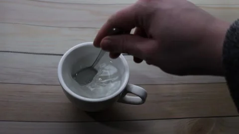 Close-up of hand stirring a white mug of liquid with a spoon on a wooden table Stock Footage 339181290