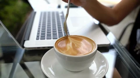 Close up of a hand stirs with spoon fresh coffee with latte art. 動画素材 334648717