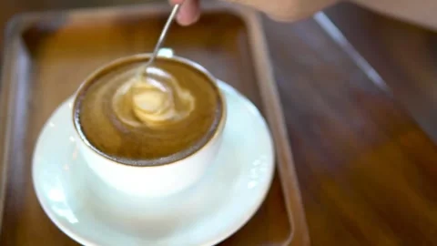 Close up of a hand stirs with spoon fresh coffee with latte art. Stock-Footage 334648724