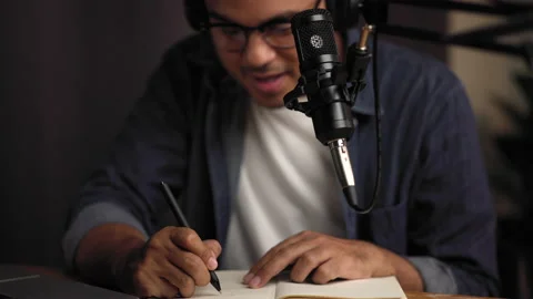 Close up hand take notes host streaming his a podcast on laptop with headphones. Stock Footage 186484268