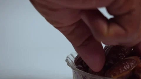 Close up hand takes dates fruit in a transparent glass bowl, isolated white Stock Footage 287681881