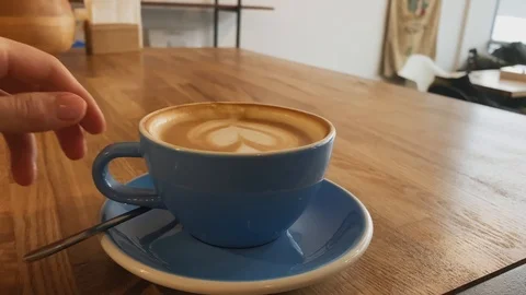 Close up of hand taking coffee of blue cup on wood table. Coffee art latte cup Stock Footage 123553243
