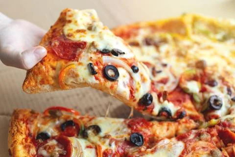 Close up of hand taking a large piece of cheesy pizza with olives Stock Photos