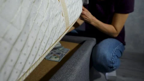 Close-up of a hand taking a stack of US dollar bills under a mattress bed. .. Stock Footage 310007731