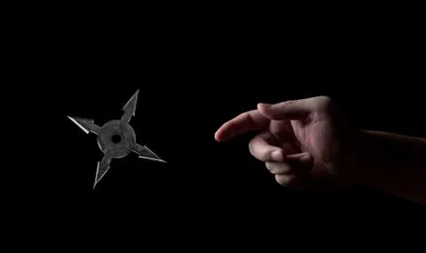 Close up Hand Throwing Ninja Star Shuriken Isolated on Black Background Stock Photos