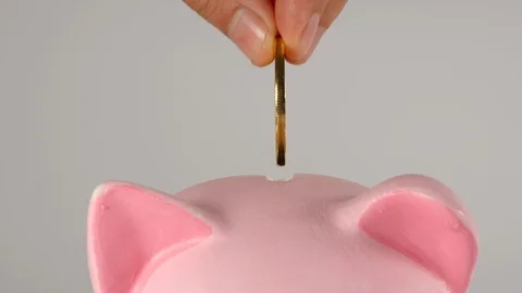 CLOSE UP: Hand throws coin into a pink piggy moneybox Видео 126005134