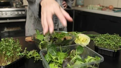 Close-up of a hand tossing arugula and spinach salad leaves into a bowl while Stock Footage 300565261