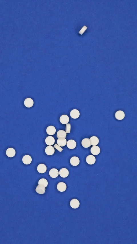 Close-Up Of A Hand Tossing Small White Pills Onto A Vibrant Blue Surface, Highli Stock Footage 314669686