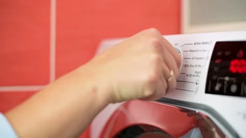 Close-up of hand turning dial on washing machine to select cycle, illustrating Stock Footage 291621016