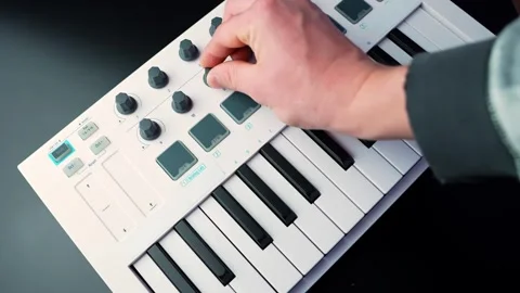 Close-up of a hand turning a knob on a white MIDI keyboard controller, shallow Stock Footage 331112336