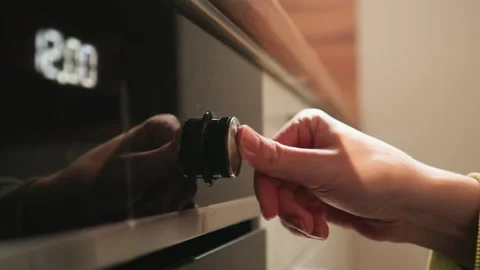 Close-up hand turning oven control knob in warm kitchen interior with shallow Stock-Footage 343539535