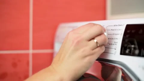Close-up of hand turning settings dial on modern washing machine in a tiled Stock-Footage 289699378