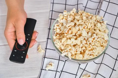 Close-up of hand with TV remote control and popcorn. Movie night at home Stock Photos