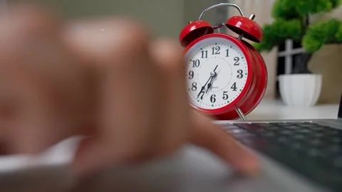 Close-up of a hand typing on a laptop with a red alarm clock in the backgroun Stock Footage 318056901