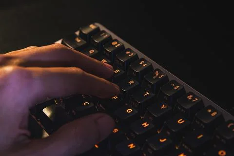 Close-up of a hand typing on a mechanical keyboard with orange backlit keys. Stock Photos