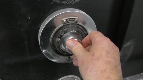 Close up of a hand unlocking a safe door vault by turning a knob with numbers Видео 106723274