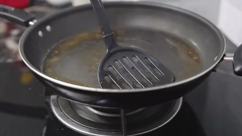 Close-up of a hand using a black spatula to stir cooking oil in a non-stick.. Stockbeeldmateriaal 340004023