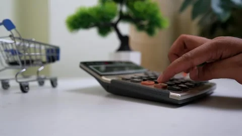 Close-up of a hand using a calculator on a desk with a small shopping cart .. Stock Footage 316799991