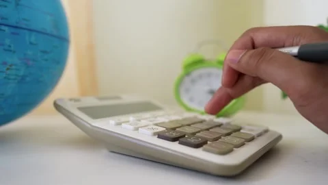 Close-up of a hand using a calculator with a globe and clock in the backgroun Stock Footage 317737092