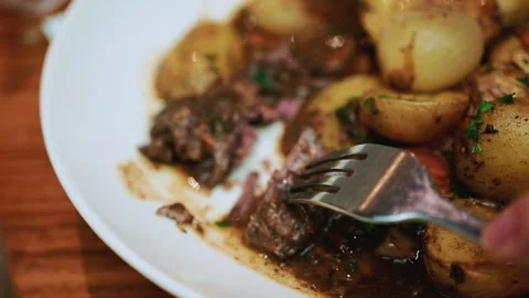 A close up of a hand using a knife and fork to cut into tender pieces of beef in Stock Footage 325803842