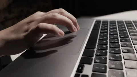 Close-up of a hand using a laptop touchpad and keyboard in a dimly lit Stock Footage 339174461