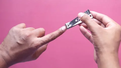 Close up of hand using nail clippers to trim fingernail on pink background,.. Vídeos de archivo 333151921