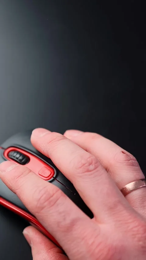 Close-up of a hand using a red and black computer mouse on a dark desk with Stock Footage 329002429
