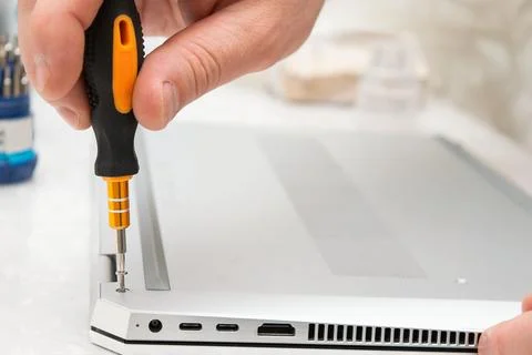 Close-up of a hand using a screwdriver to repair a laptop, with visible por.. Stock Photos