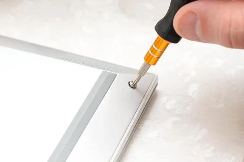 Close-up of a hand using a screwdriver to tighten a screw on a silver lapto.. Stock Photos