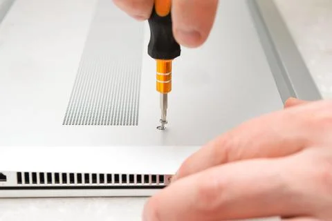 Close-up of a hand using a screwdriver to tighten a small screw on a silver.. Stock Photos