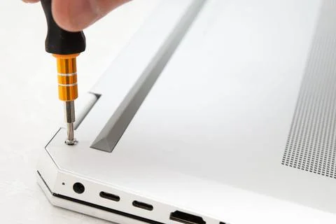 Close-up of a hand using a screwdriver to tighten a screw on a silver lapto.. Stock Photos