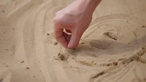 Close-up of a hand using a small object to draw circular shapes in beach sand Stock Footage 343381421