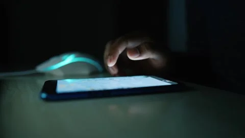 Close-up of a hand using a smartphone in a dark room, with a glowing mouse .. Stock Footage 317736860