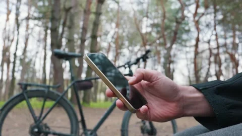 Close Up of Hand Using Smartphone in Forest Near Blurred Bicycle Vídeo Stock 334125105