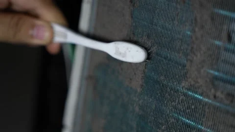 Close-up of a hand using a toothbrush to clean dust from a dirty air condit.. 動画素材 338319382
