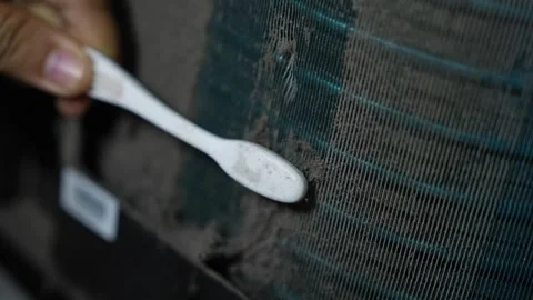Close-up of a hand using a toothbrush to clean dust from an air conditioner.. Stockbeeldmateriaal 338319392