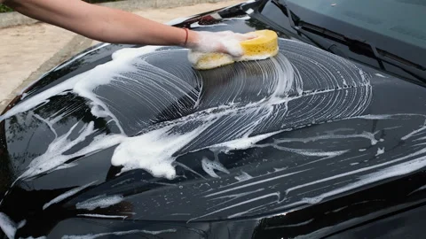Close-up of a hand washing a black car with a soapy sponge, creating rich foam Stock Footage 341739643