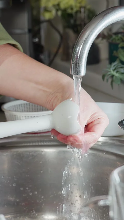 Close up of hand washing white kitchen utensil with pink residue under running Stock Footage 344424558