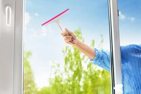 Close-up of a hand washing a window with a squeegee against a bright sunny .. Stock Photos