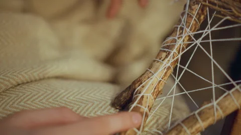 Close up of hand weaving white string around wooden sticks to create intricate Stock Footage 347990639