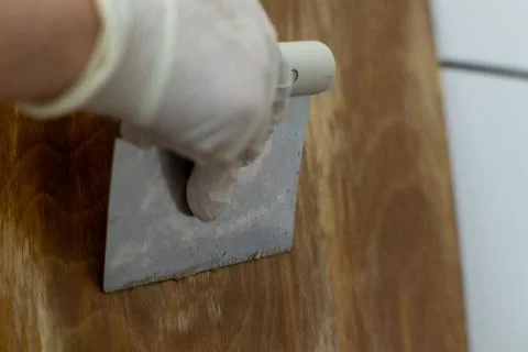 Close-up of a hand in a white glove using a metal putty knife to smooth woo.. Stock Photos