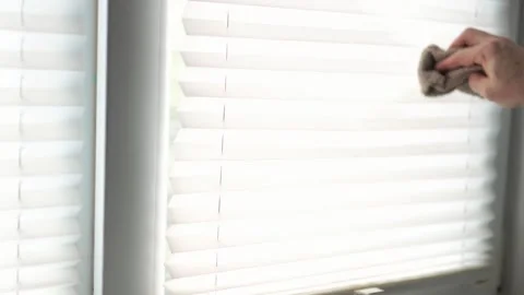 Close up of a hand wiping dust from white pleated window blinds with a rag 動画素材 340159366