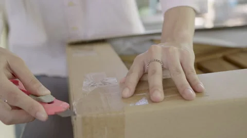 Close-up Hand of woman using a cutter to unpack a box containing a wooden chair. Video stock 331845379