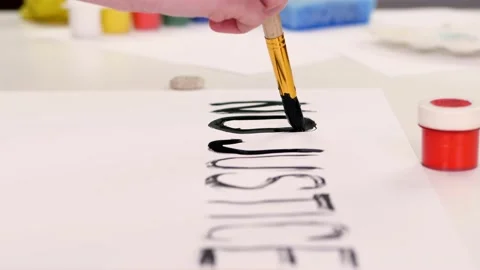 Close-up, hand writes slogan with brush, using black watercolor paint on white Stock Footage 132325779