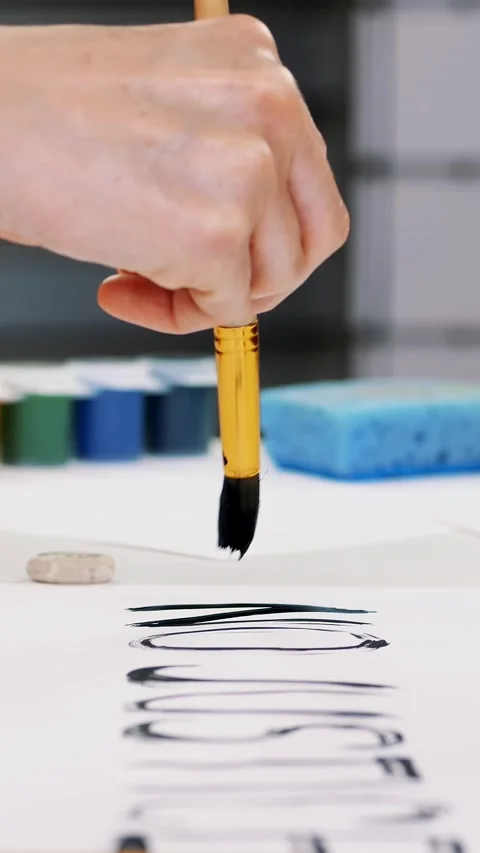 Close-up, hand writes slogan with brush, using black watercolor paint on white Stock-Footage 319940734