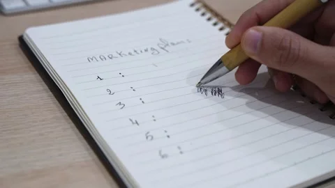 Close-up hand writing marketing plan strategy notes in spiral notebook on Stock Footage 332120680